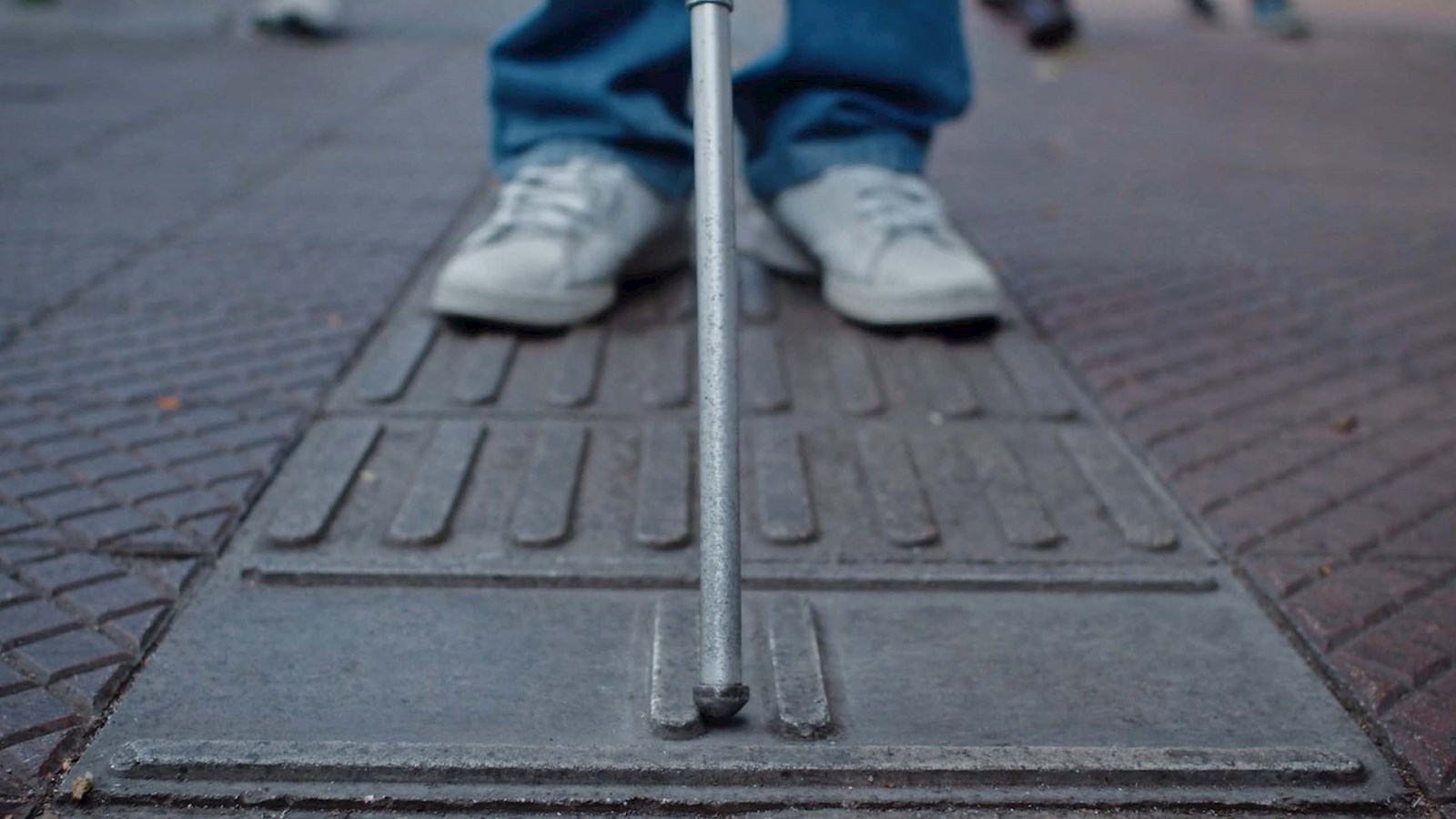 Ground level shot of a person with a walking stick for blind and partially sighted people using the pavement pattern developed by Cemento Sol to establish where they are on the street