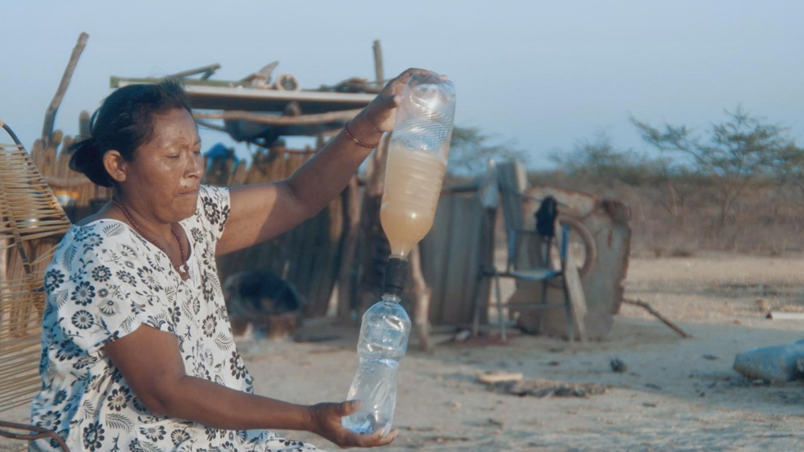 A lady wearing a white patterned dress using a FILSA filter cap to turn dirty water into drinking water