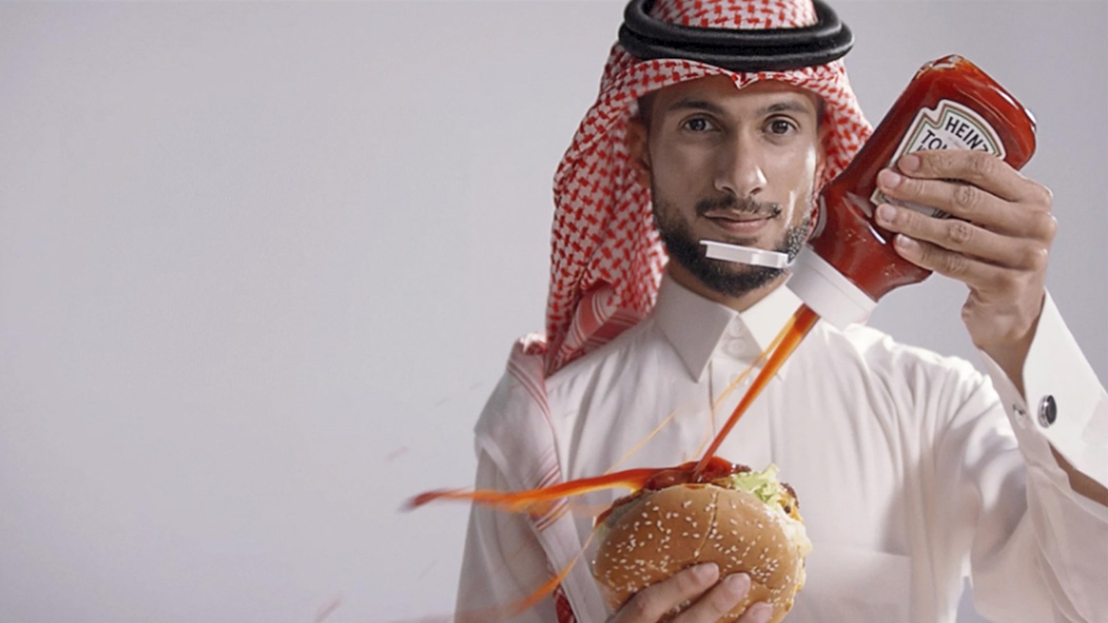 Man dressed in a thobe squirting Ketchup onto a burger